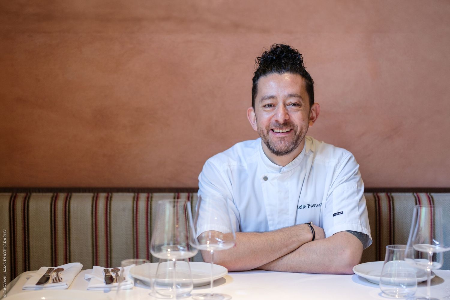 Chef leaning against colorful storefront window during daytime.