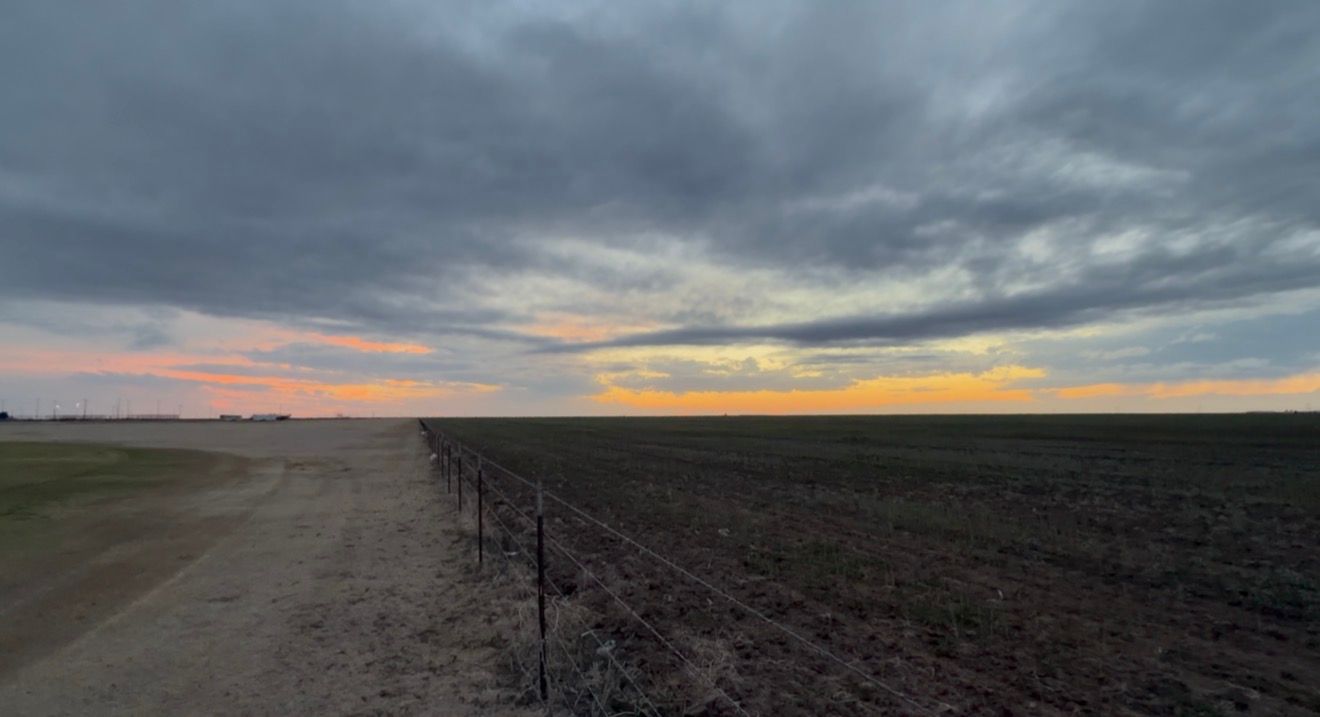 Dramatic sunset over vast plowed farmland with dark storm clouds and colorful horizon in rural countryside.