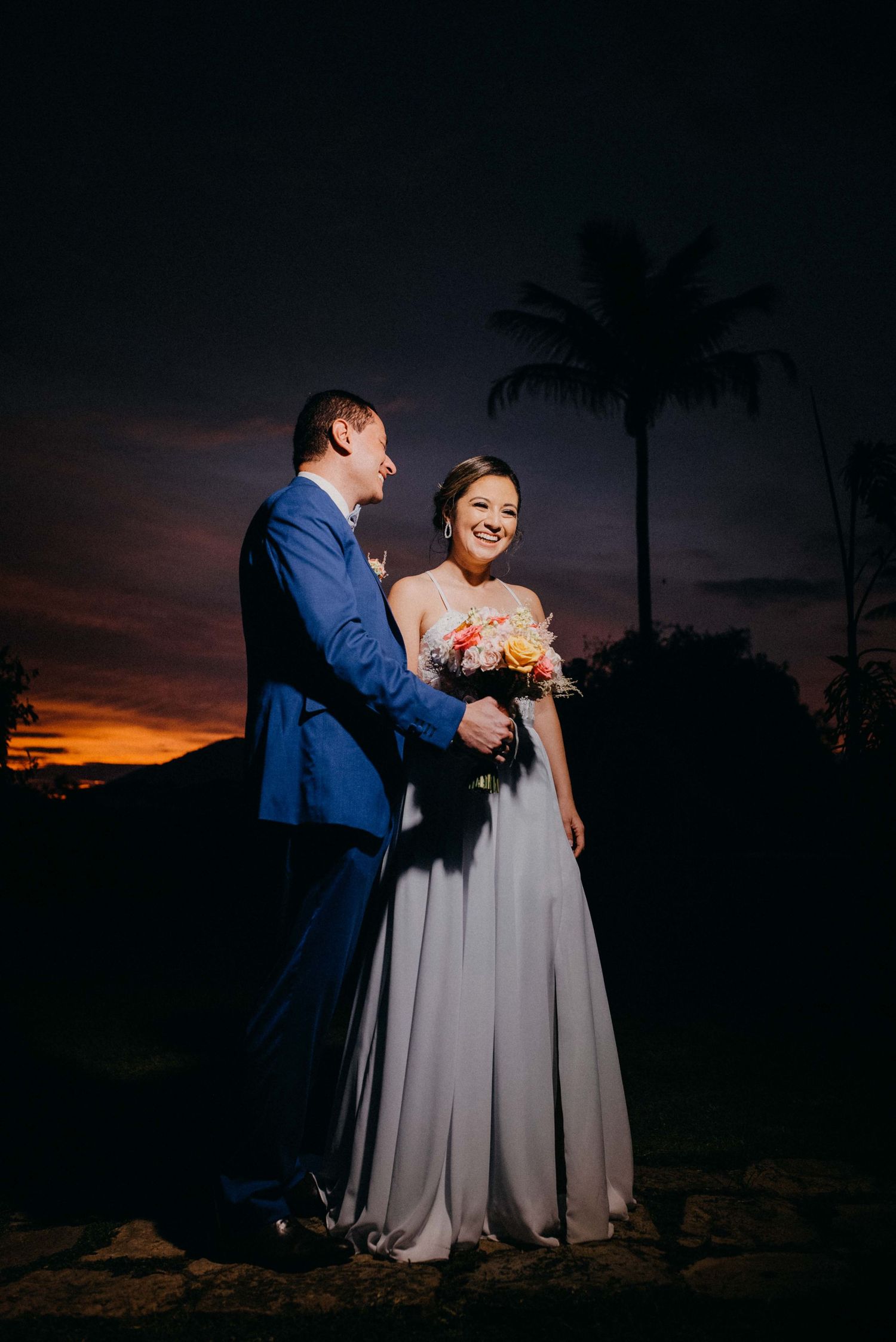 Bride and groom share a romantic sunset moment surrounded by palm trees in a stunning tropical wedding portrait.