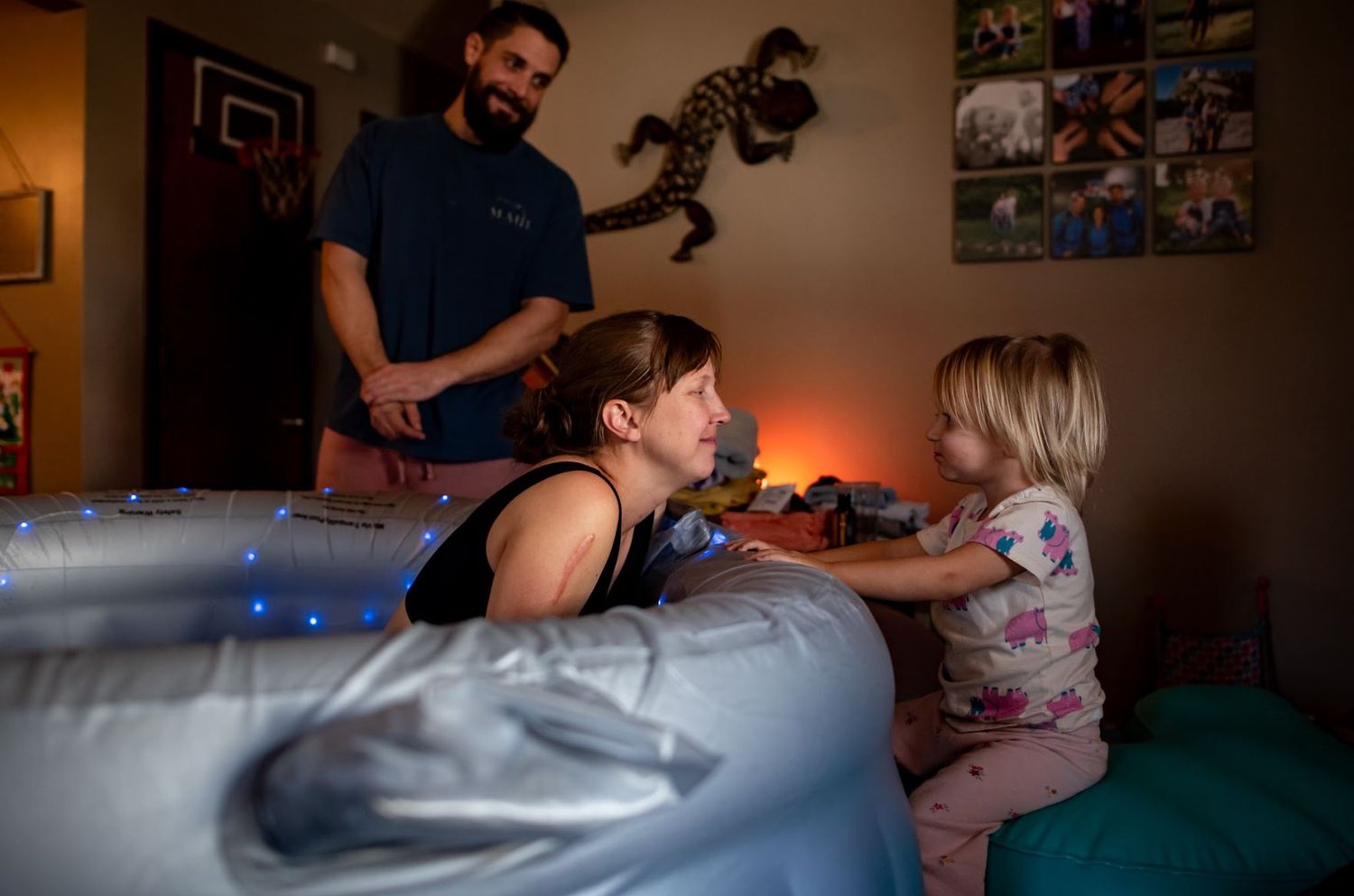 Family shares a playful moment together on an inflatable mattress in a dimly lit room with wall decorations.