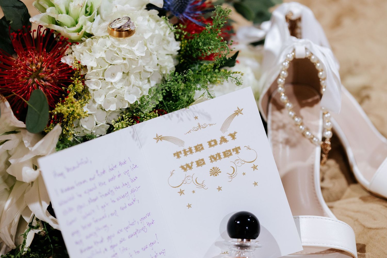 Handwritten wedding vows and rings displayed alongside elegant white and red floral arrangements on a light surface.