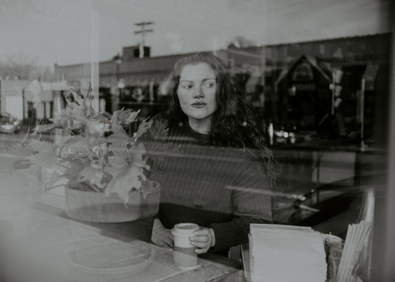 A vintage black and white photograph shows someone seated at a table near a window.