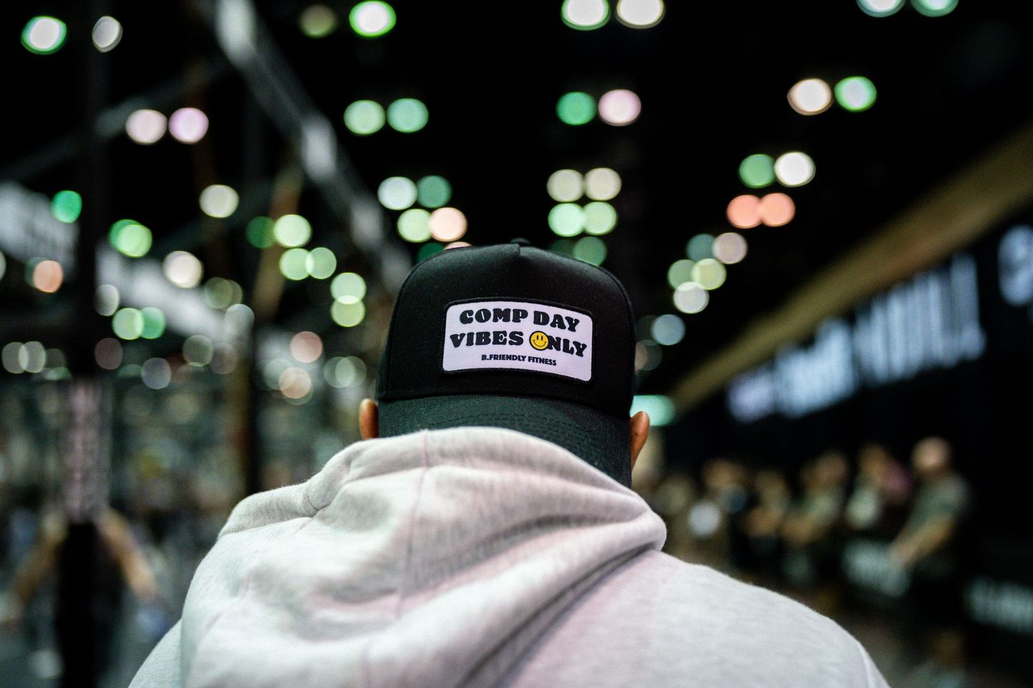 Person wearing a baseball cap with text in a dimly lit venue with bokeh lights in background.