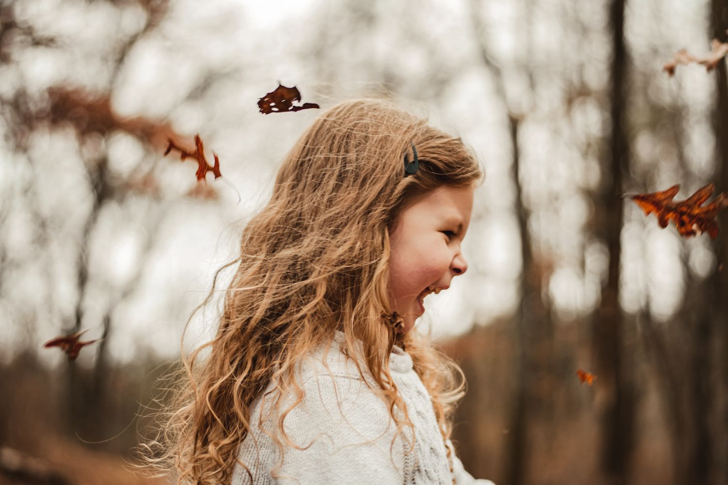 Child outdoors with windblown hair enjoying falling autumn leaves.