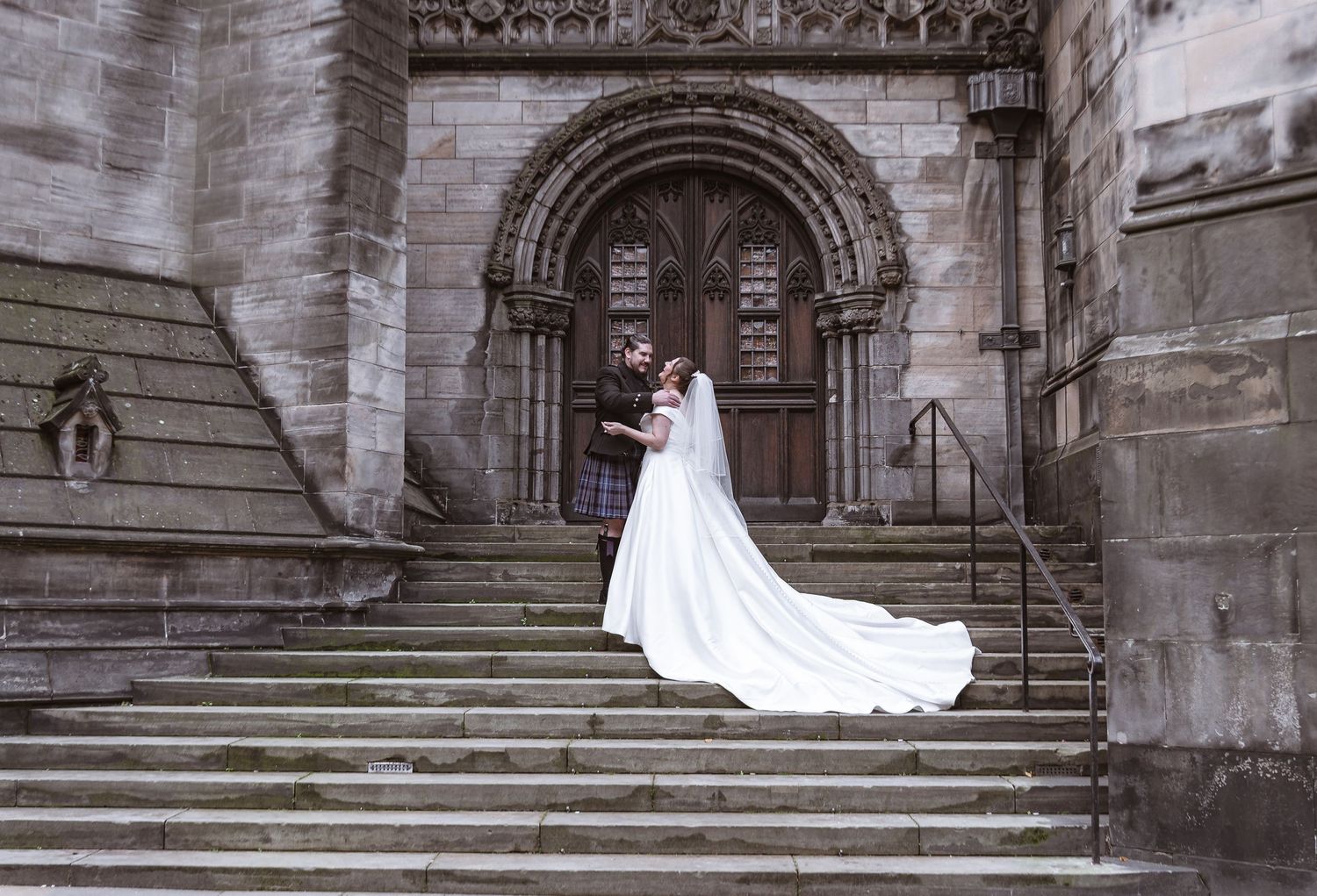 A bride in flowing white gown poses on grand stone cathedral steps.
