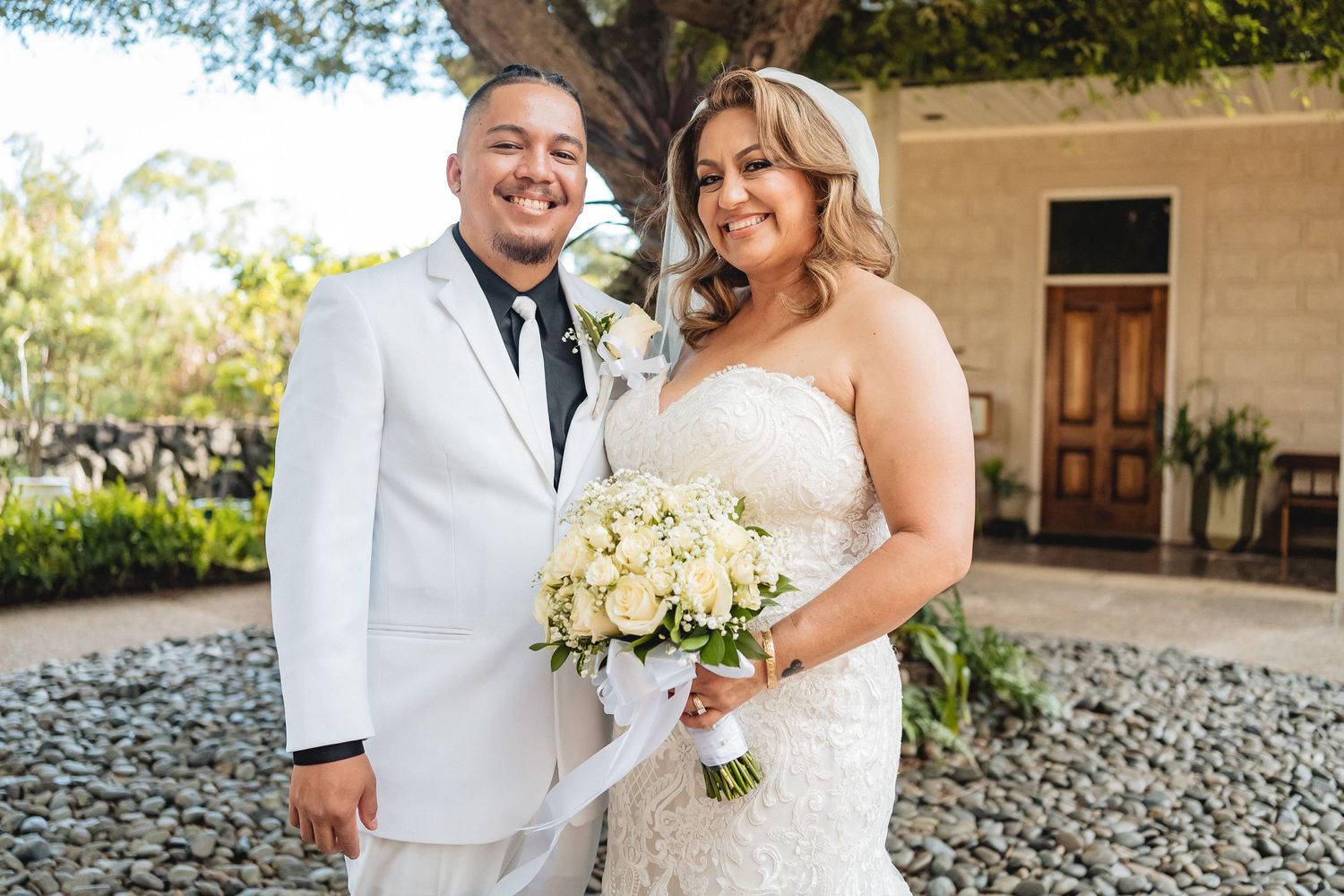 A newlywed couple poses for a portrait in formal wedding attire with white floral bouquet.
