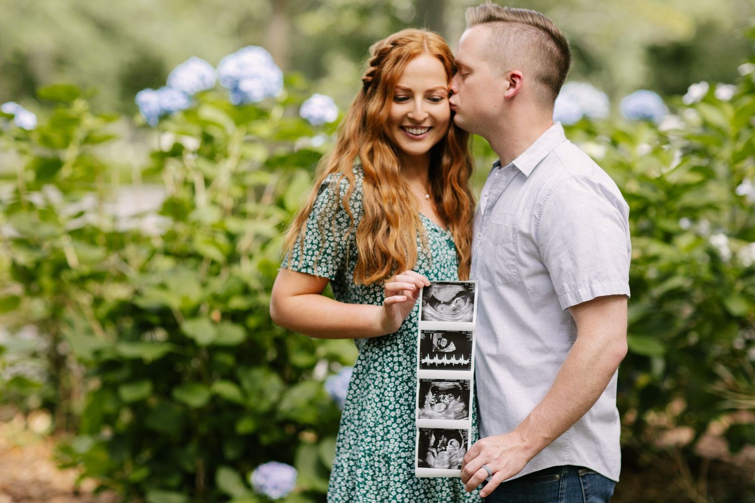 A couple sharing a joyful moment while holding a letterboard in front of hydrangea bushes.