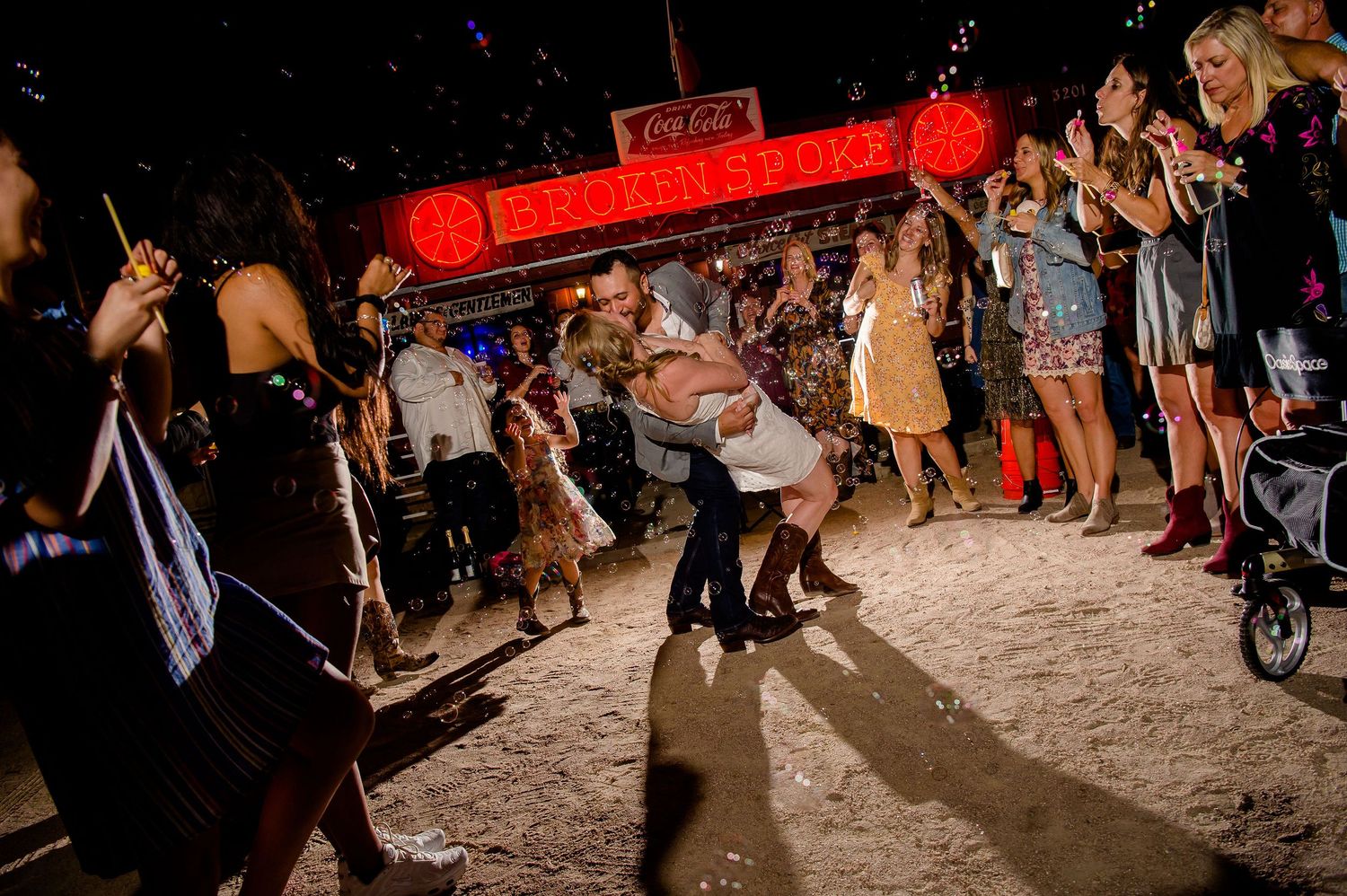 People celebrating at a nighttime event with dramatic lighting and shadows on sandy ground.