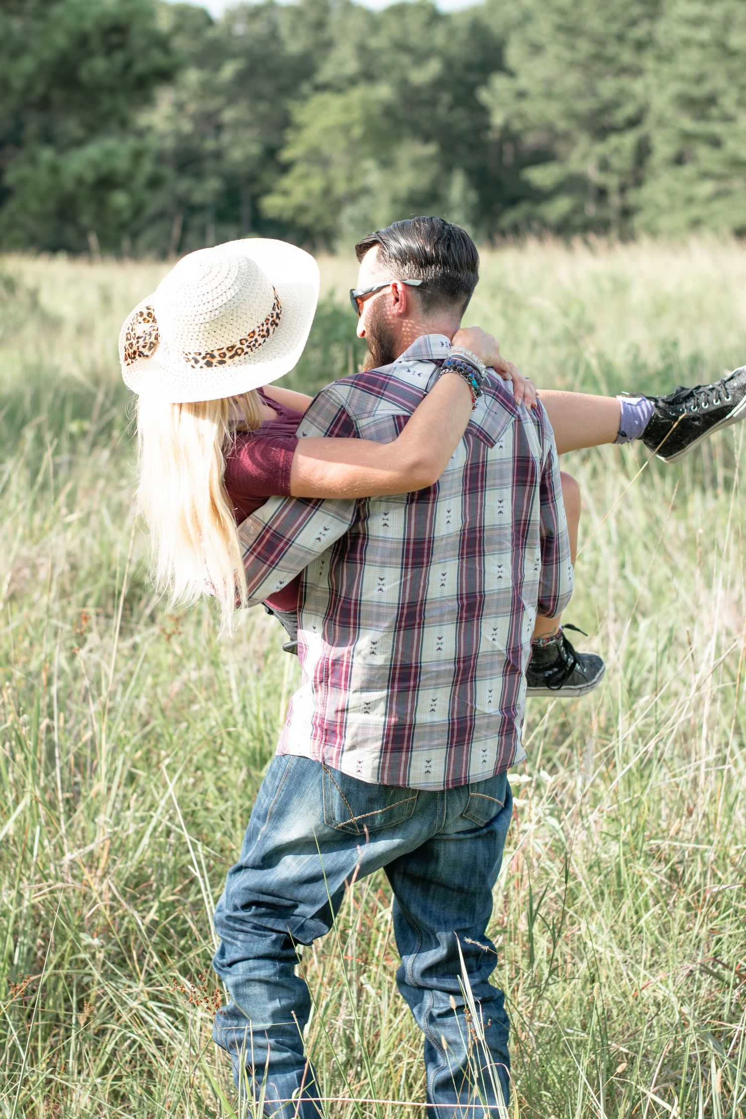 A romantic moment captured in a sunny meadow with tall grass and natural lighting.