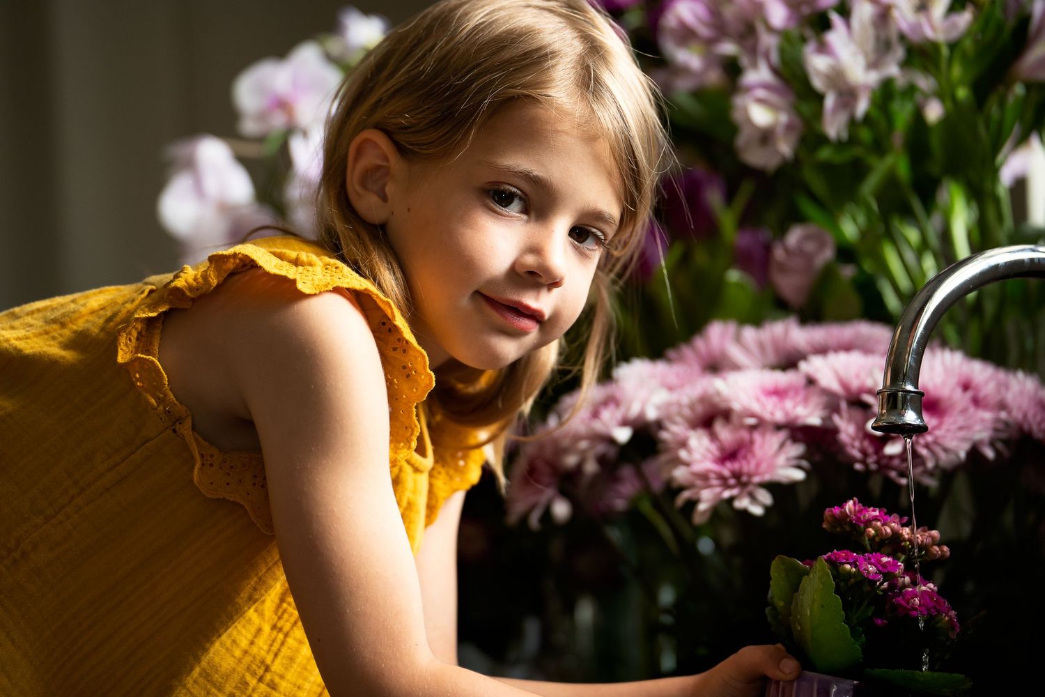 young girl in yellow dress watering a flower surrounded by flowers in home portrait session San Antonio Texas