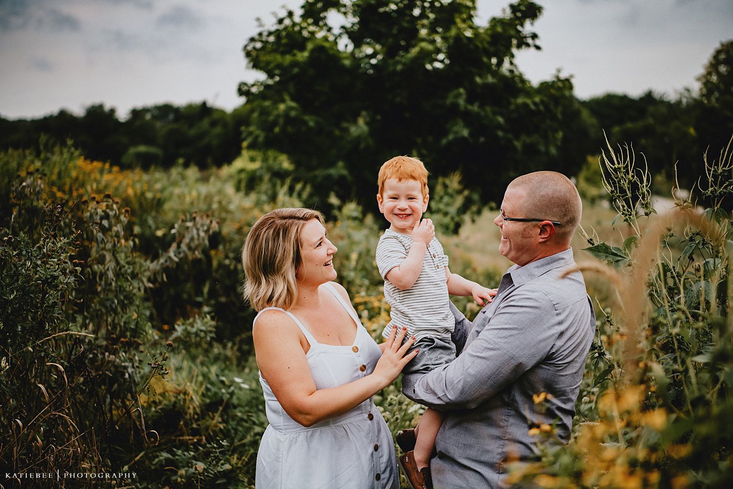 Family shares joyful moment together outdoors surrounded by lush summer greenery.