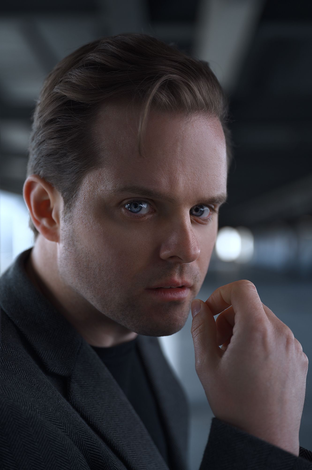 Portrait study with dark attire and contemplative pose against industrial background.