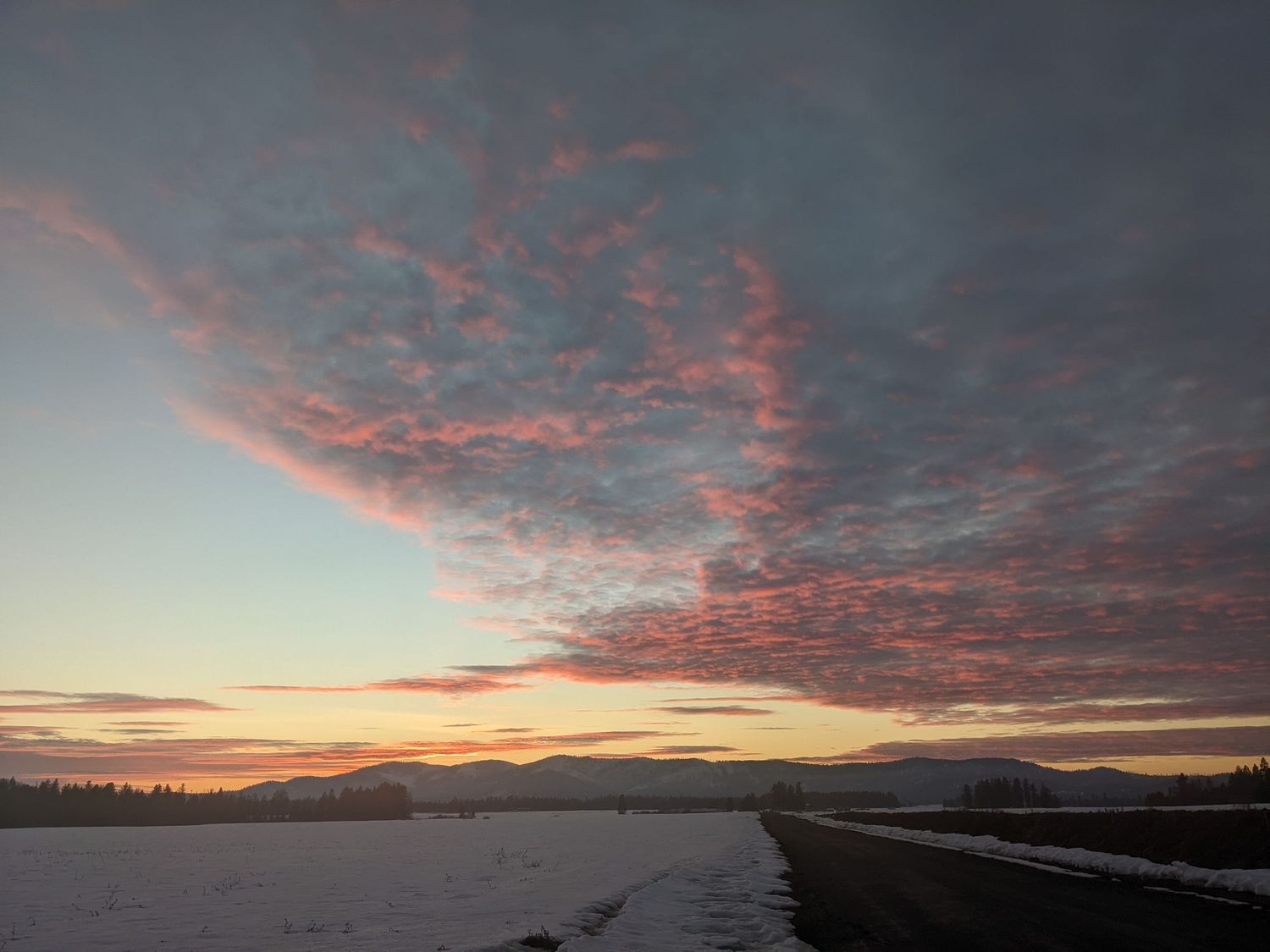 A stunning sunset with pink clouds reflecting over a snow-covered landscape.