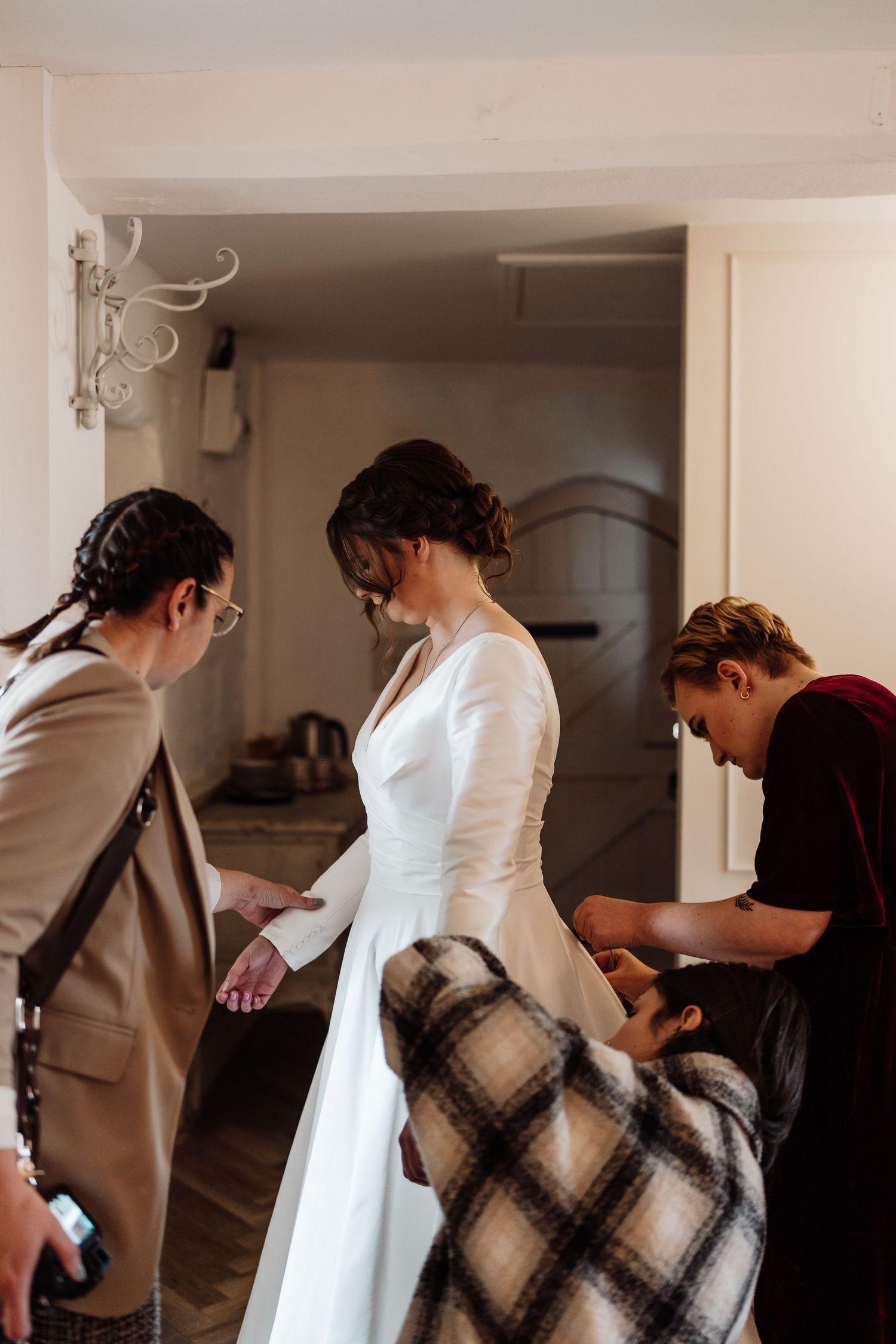 A bride is getting dressed. The photographer is helping do up the sleeve buttons.