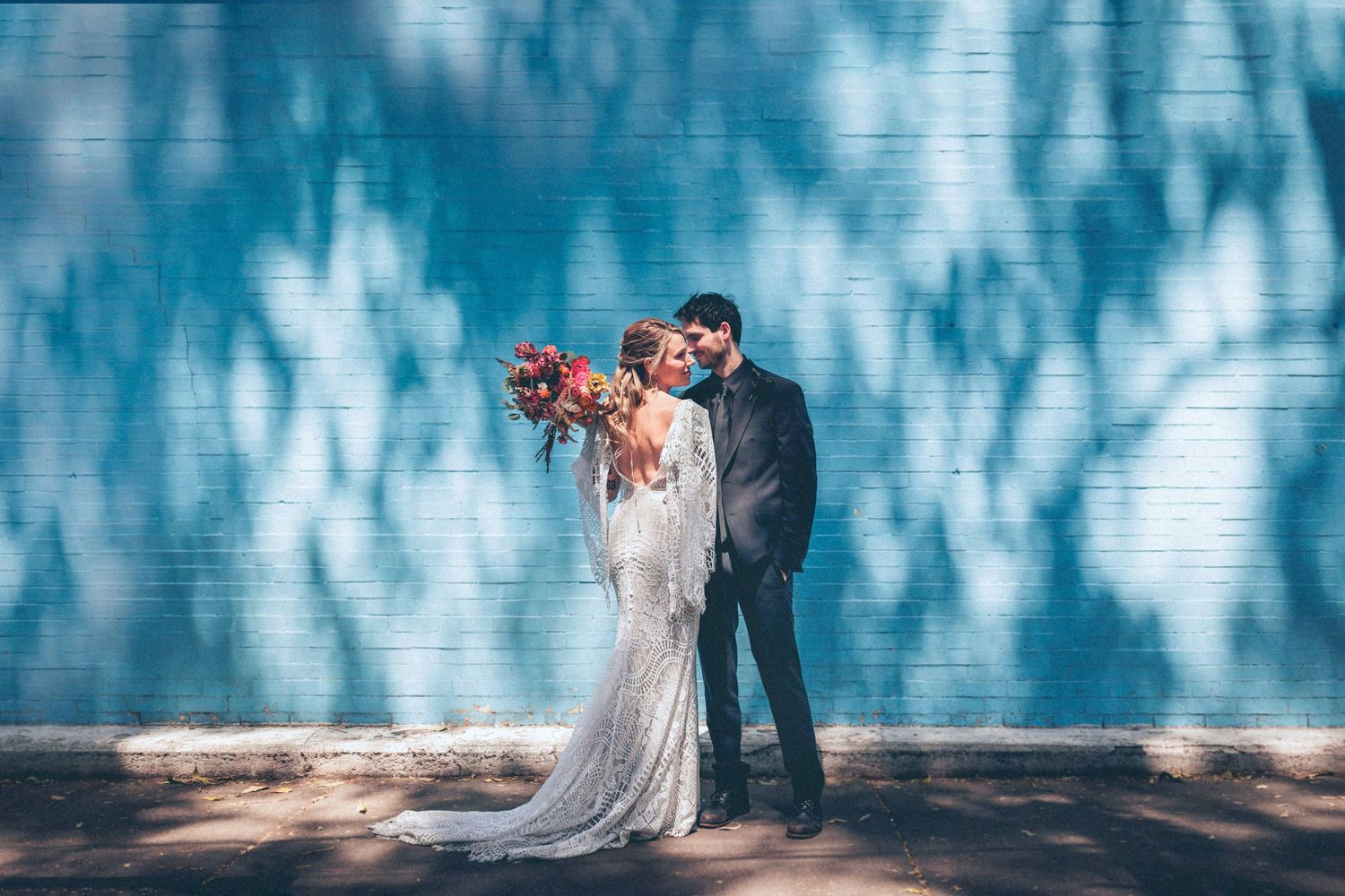 Couple posing against blue-tinted wall with dramatic shadows and flowing dress.