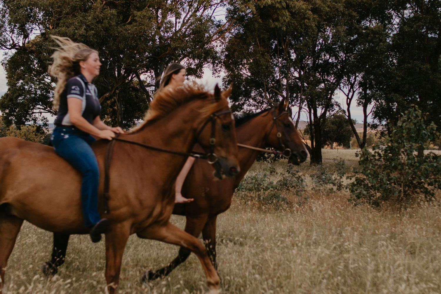 two sister riding their horses bareback through the trees with hills in the background at their property near Gundaroo.