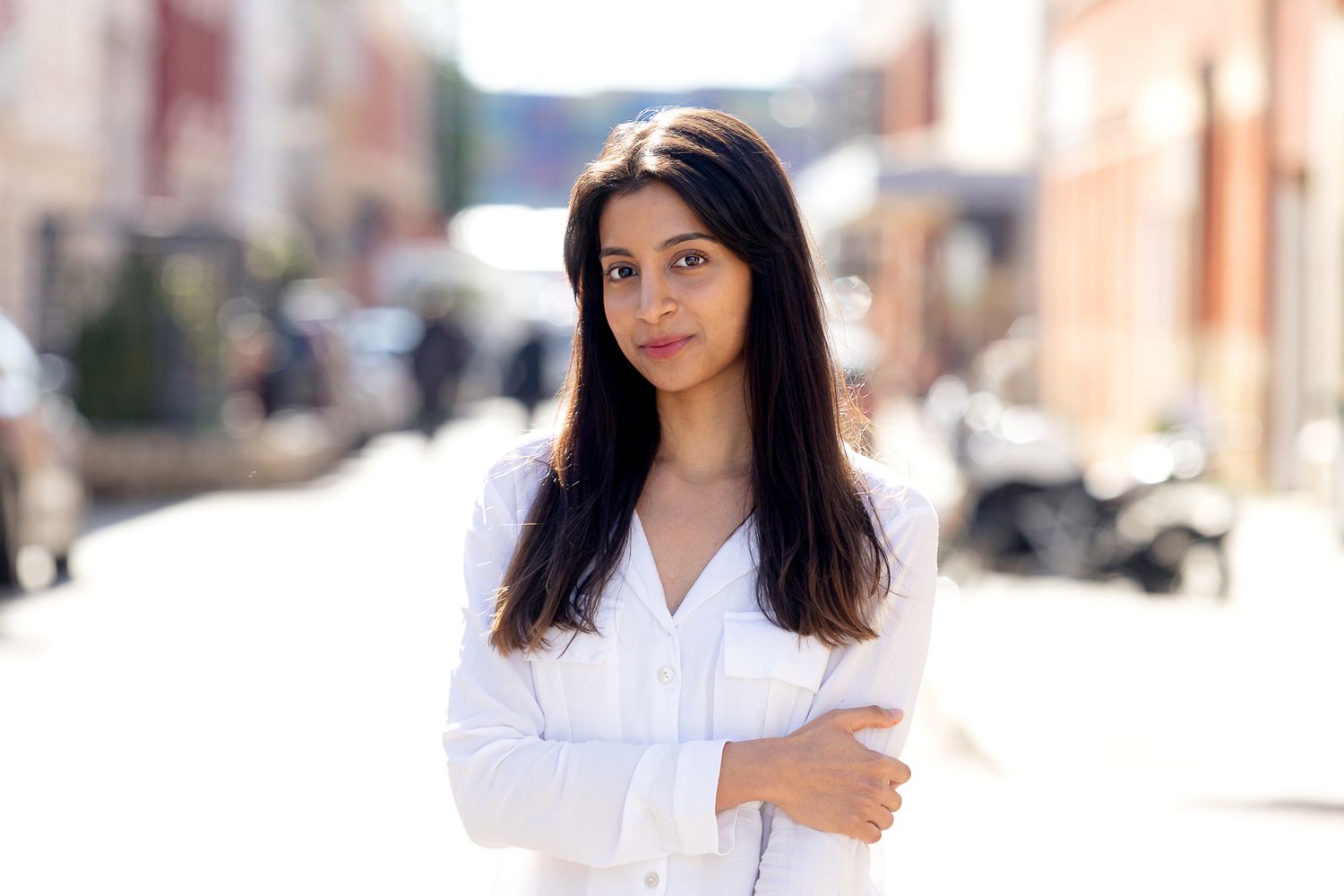 Portrait of someone in a white blouse standing confidently on an urban street.