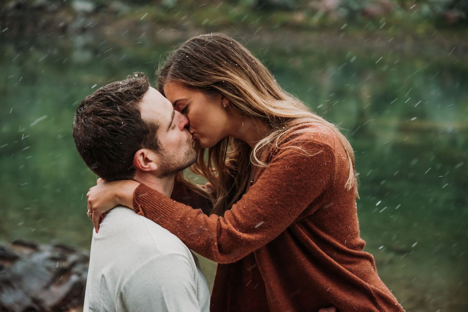 Intimate romantic moment captured by a serene mountain lake with evergreen trees in the background.