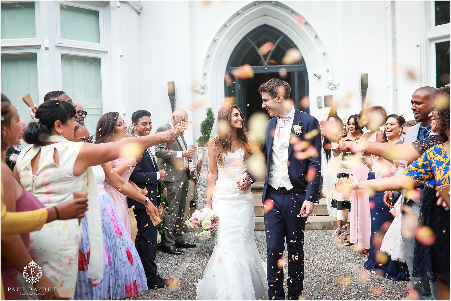 Wedding guests shower newlyweds with confetti as they exit a white church doorway.
