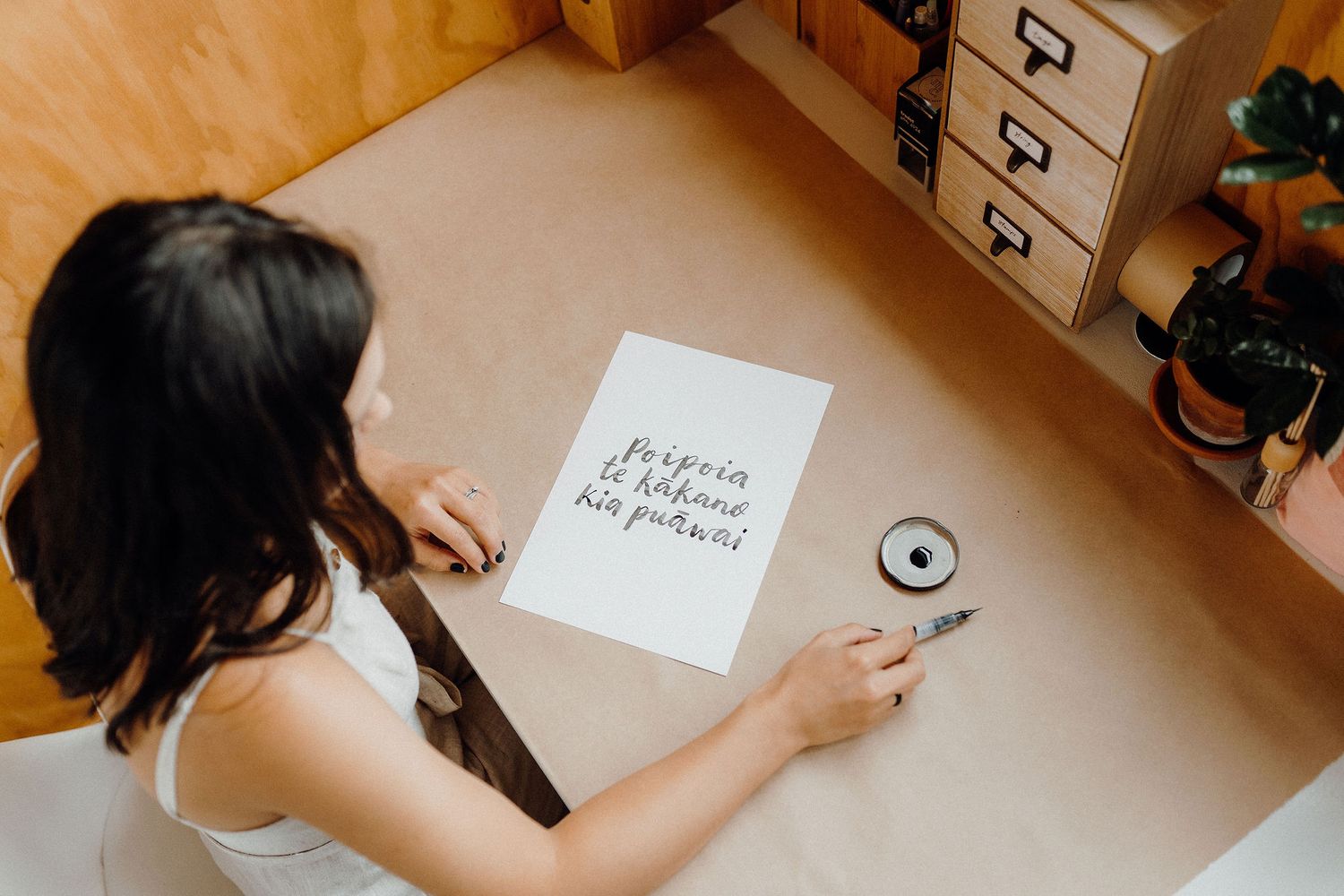 Woman writing calligraphy at desk with wooden storage boxes.