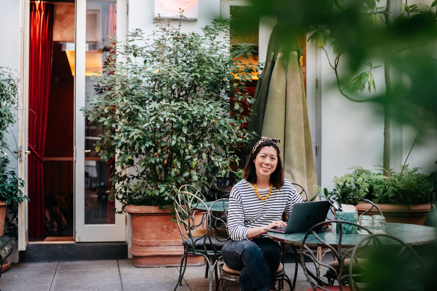 A cozy outdoor patio scene with someone working on a laptop amid greenery.