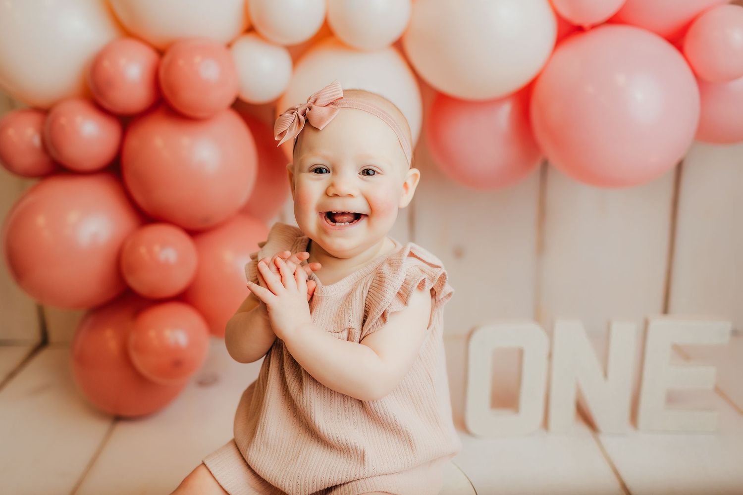 First birthday photo setup with pink balloon arch and white wooden background.