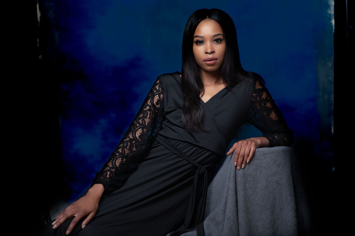 Studio portrait with black lace dress against dark blue background.