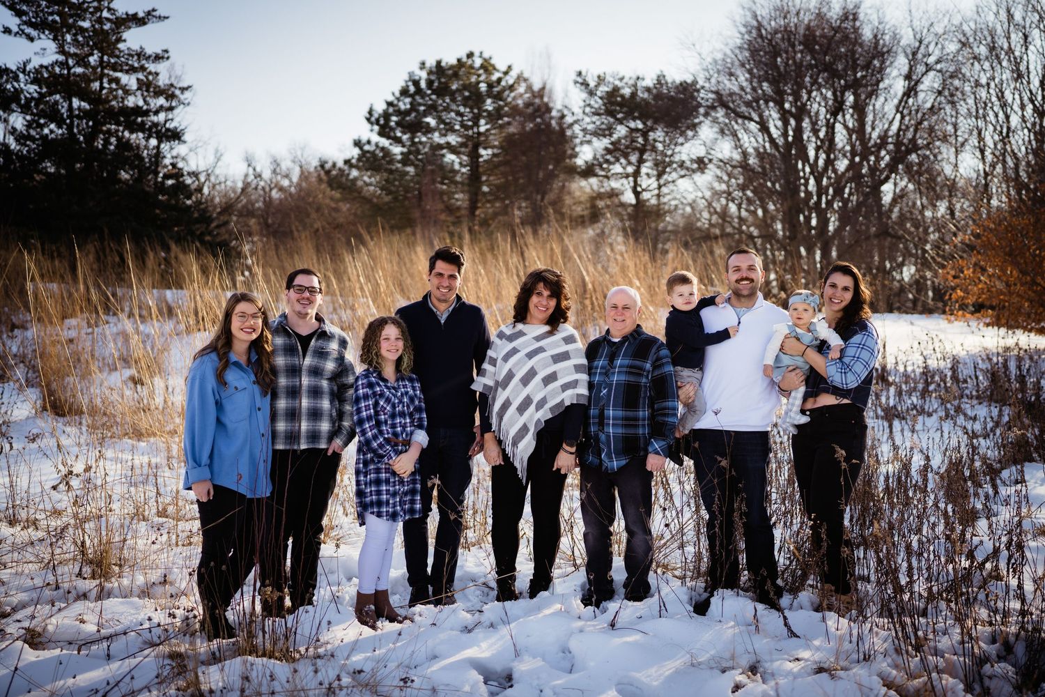Group winter family photo with people wearing coordinated blue and plaid outfits in snow.