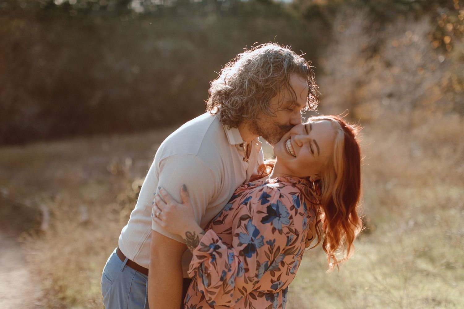 A couple shares a playful moment in golden sunset light against a natural background.