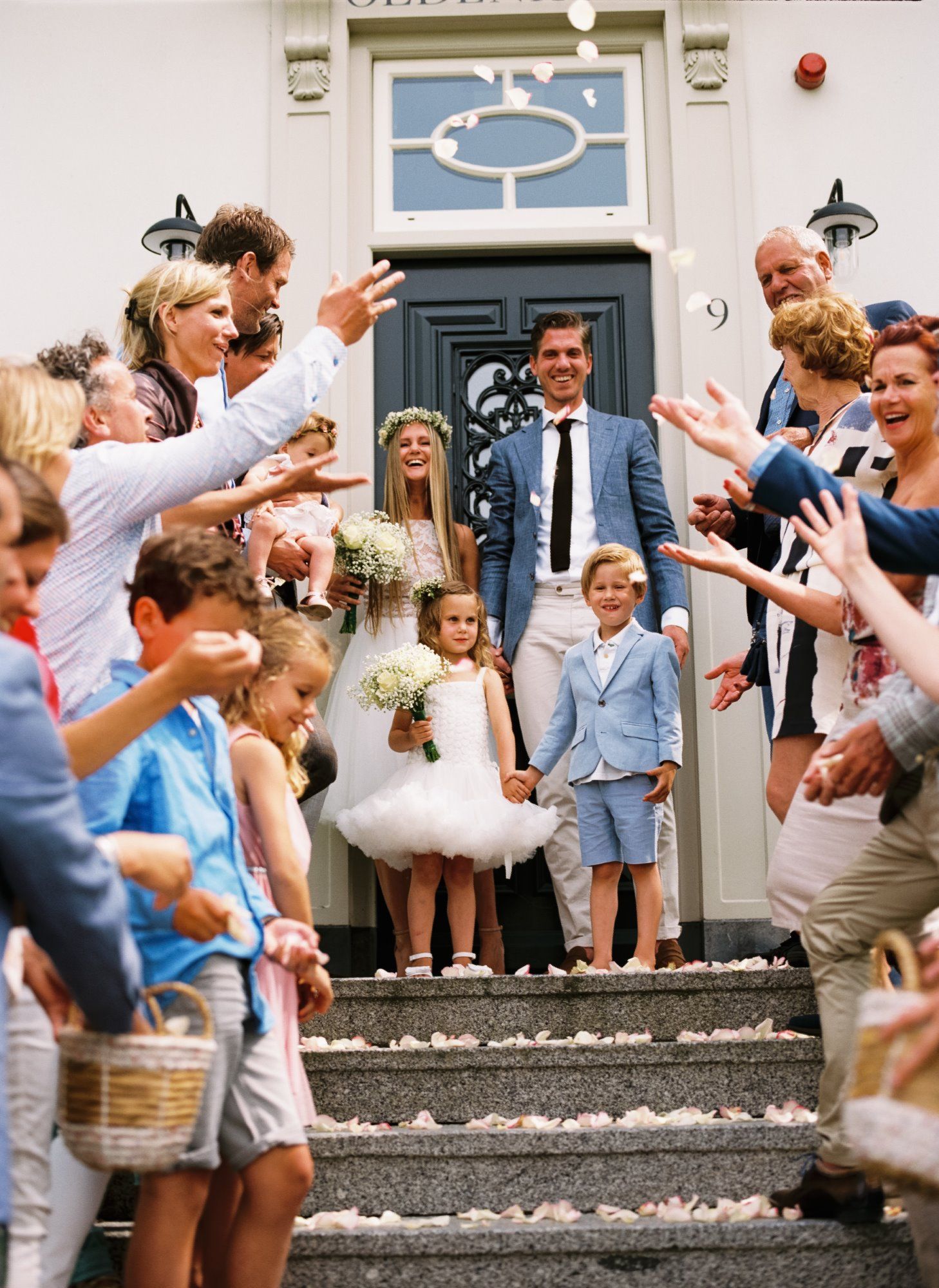 A joyous crowd throws confetti on the steps of a building with a classic blue and white doorway.