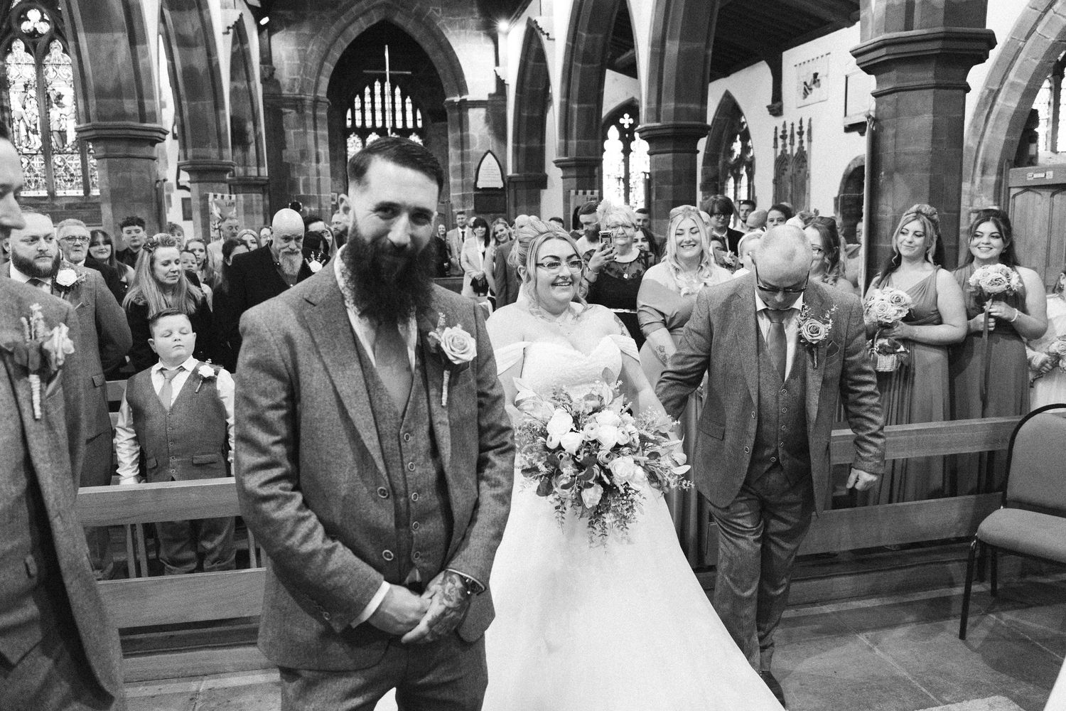 Black and white photo of a wedding ceremony in a grand church with stone arches.