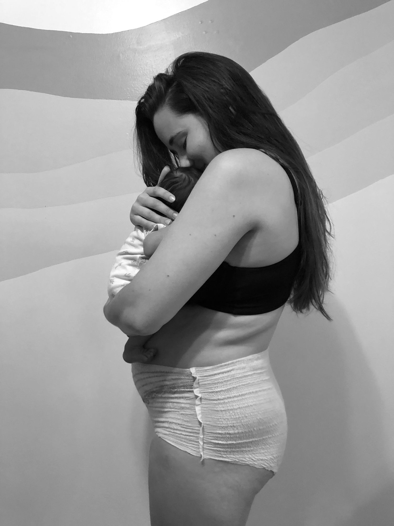 Black and white photo of a young mother holding and kissing her newborn baby.