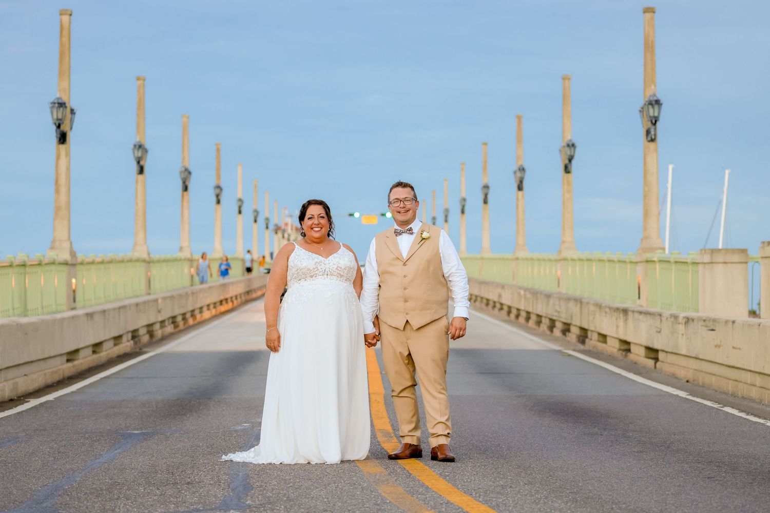 Wedding couple standing on a bridge with ornate light posts stretching into the distance.
