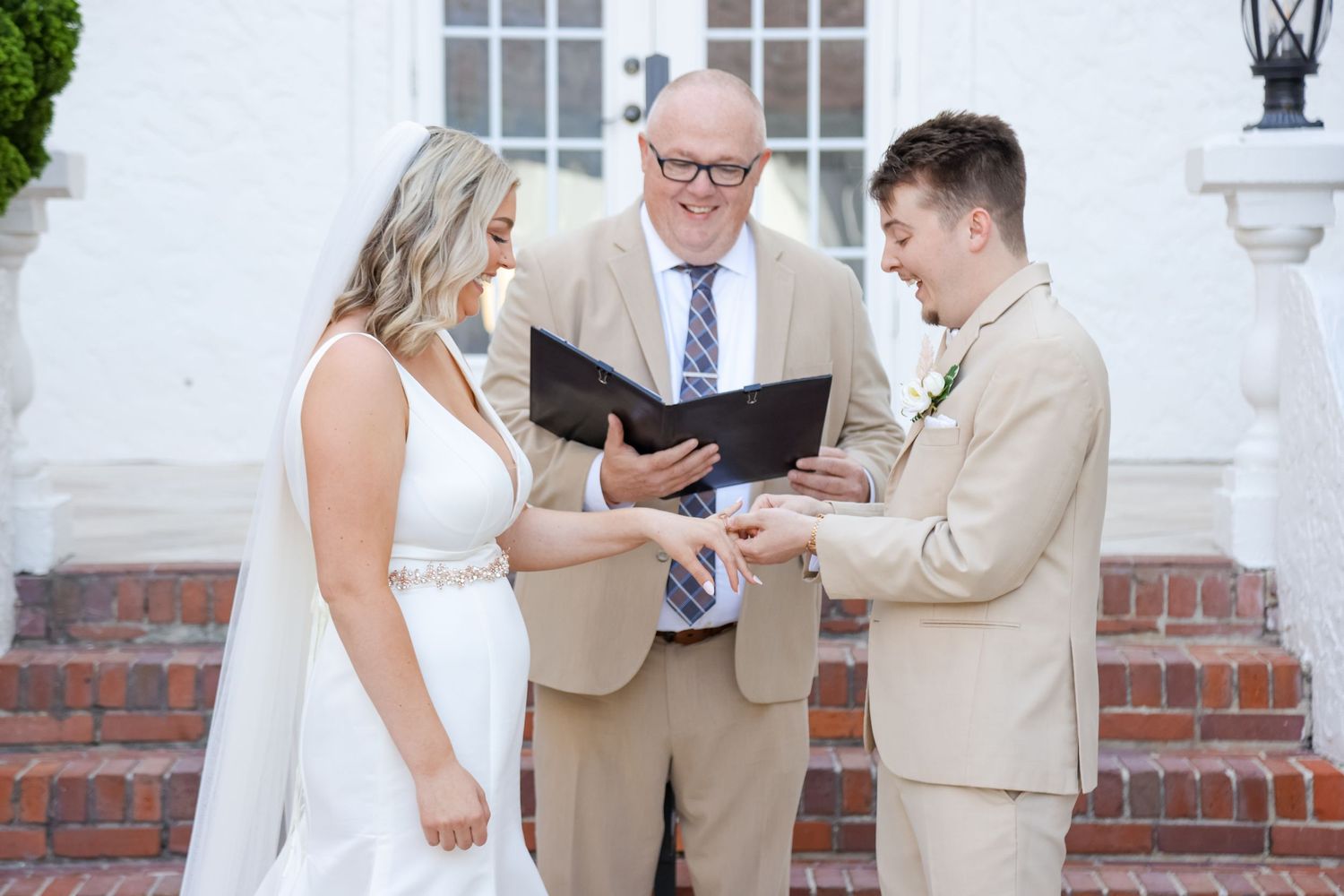 A wedding ceremony takes place on brick steps of a white colonial building.