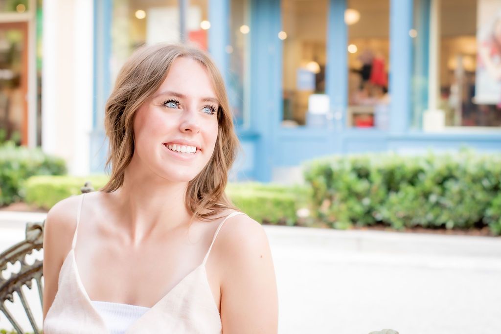 Bright outdoor portrait with blue storefronts and landscaping visible.