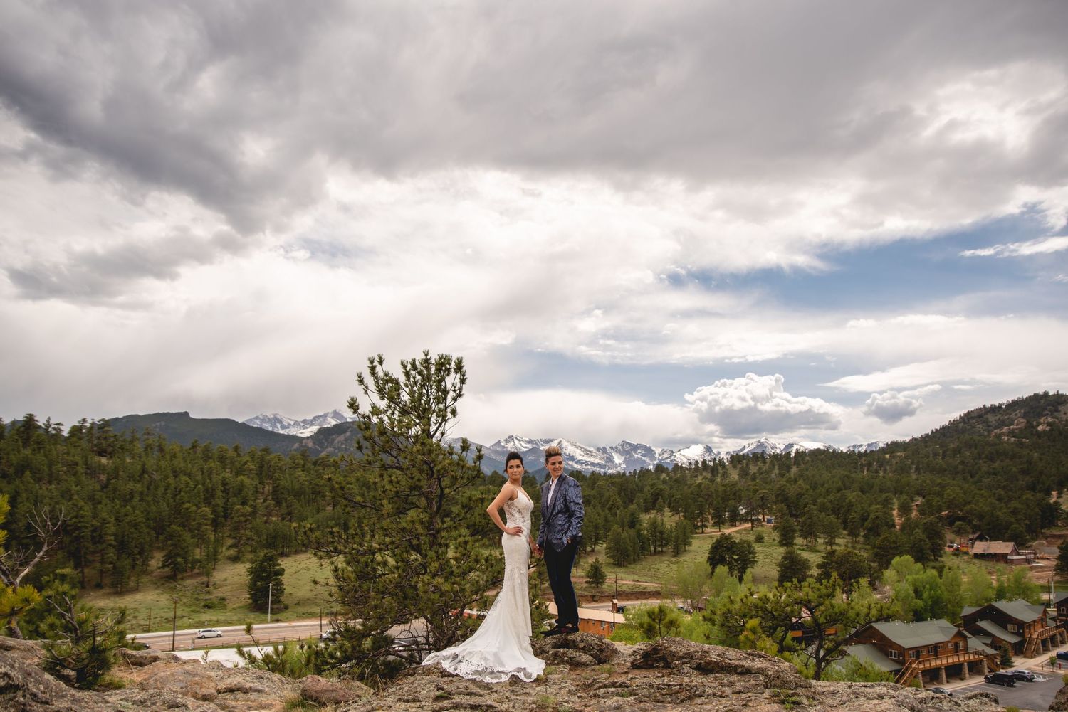 Couple embraces on a mountain overlook with dramatic cloudy skies and mountain peaks.