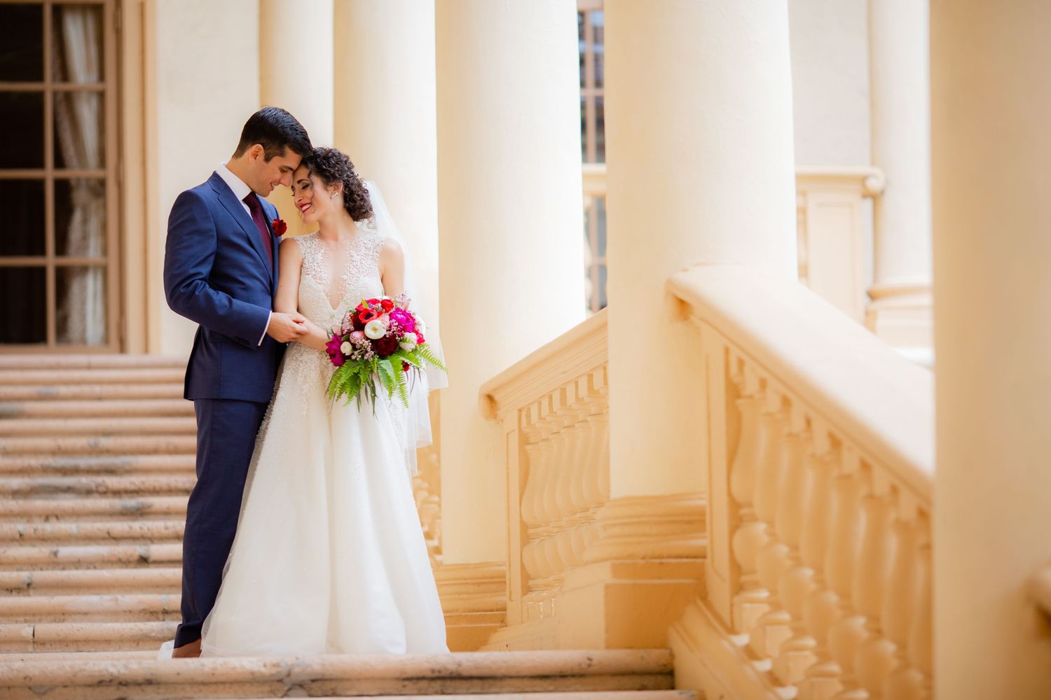 A tender wedding moment captured on an elegant staircase with classic columns.