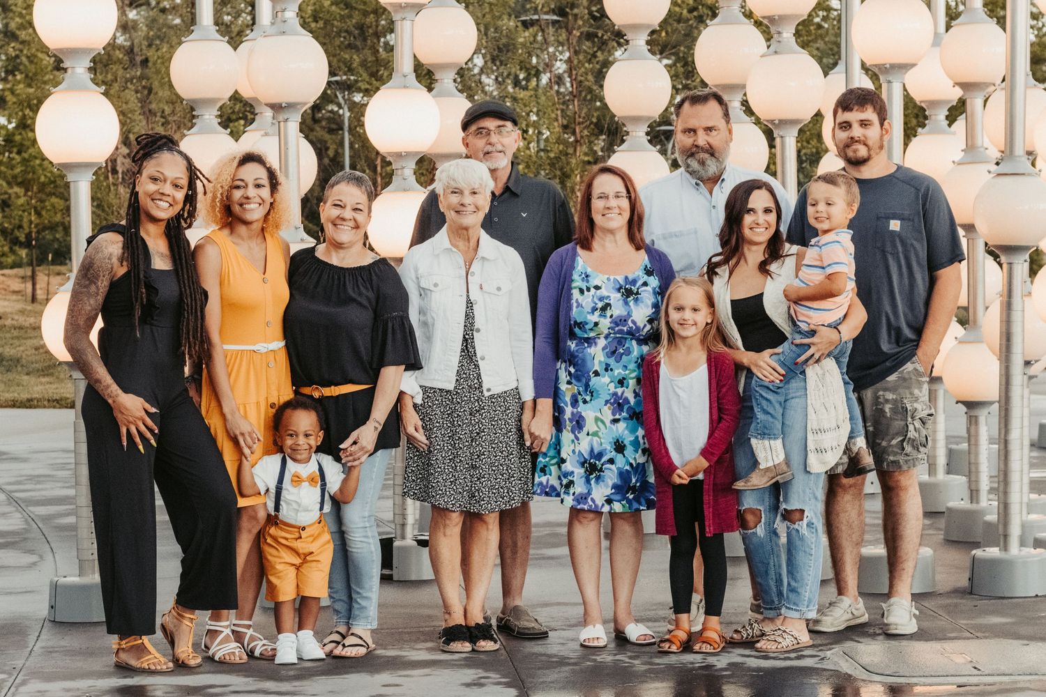 Extended family gathering poses beneath decorative white globe lights outdoors.