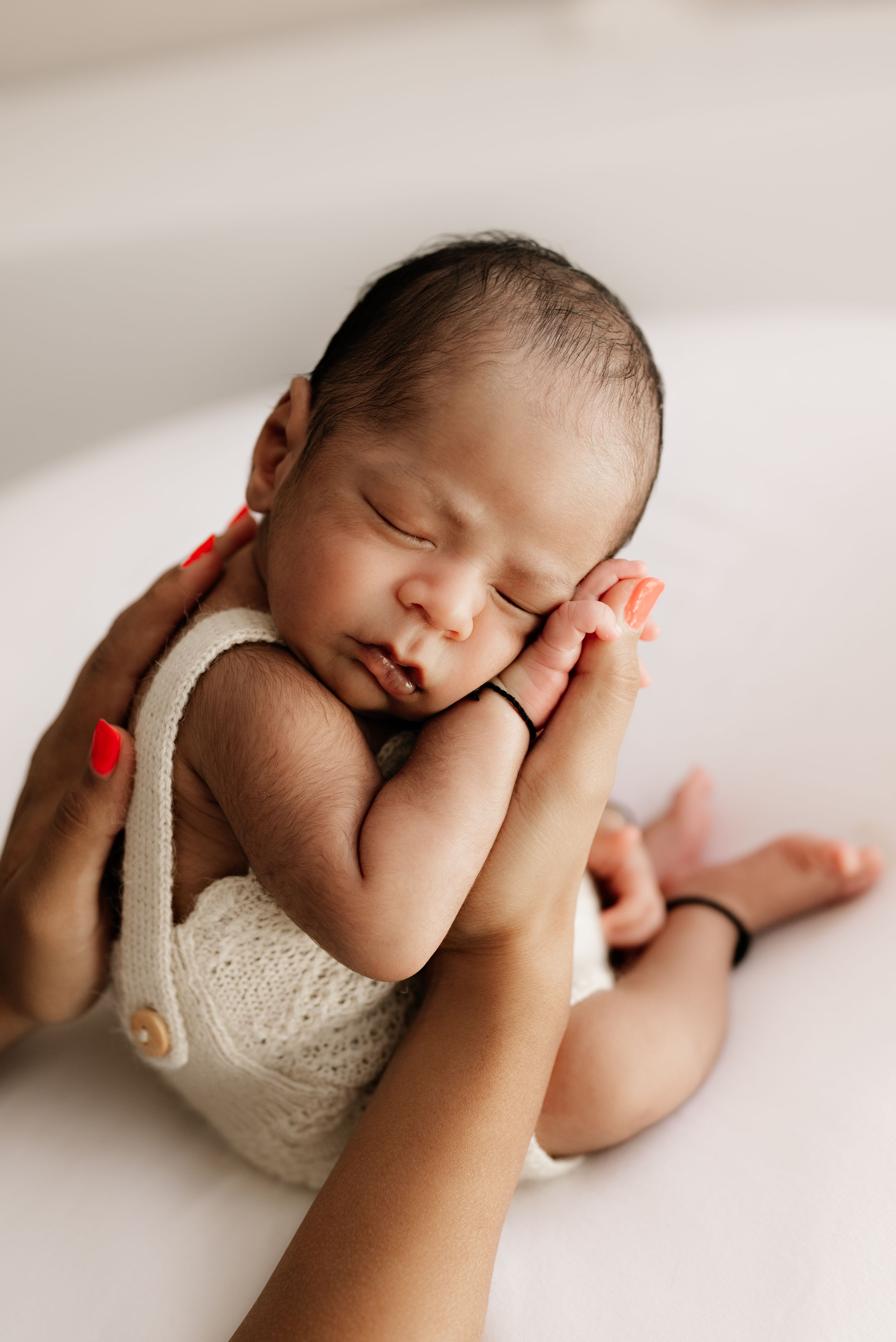 Peaceful sleeping newborn cradled in gentle hands wearing white lace outfit.