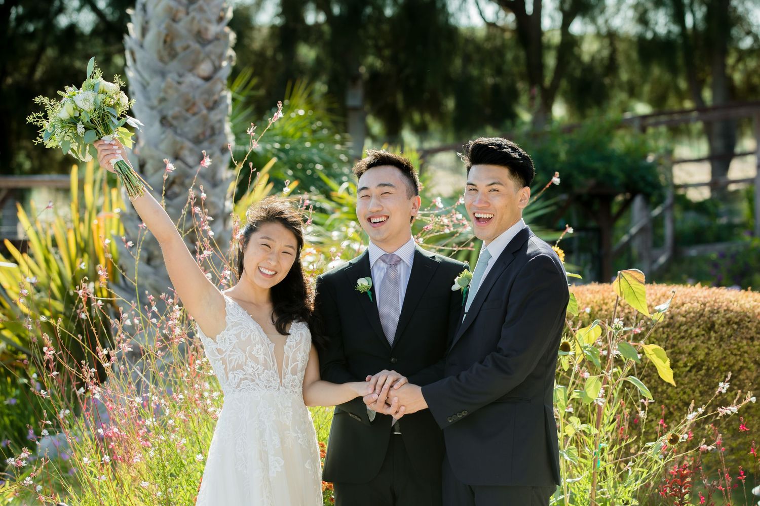 Three people celebrating joyfully in a sunny garden setting with lush greenery in the background.