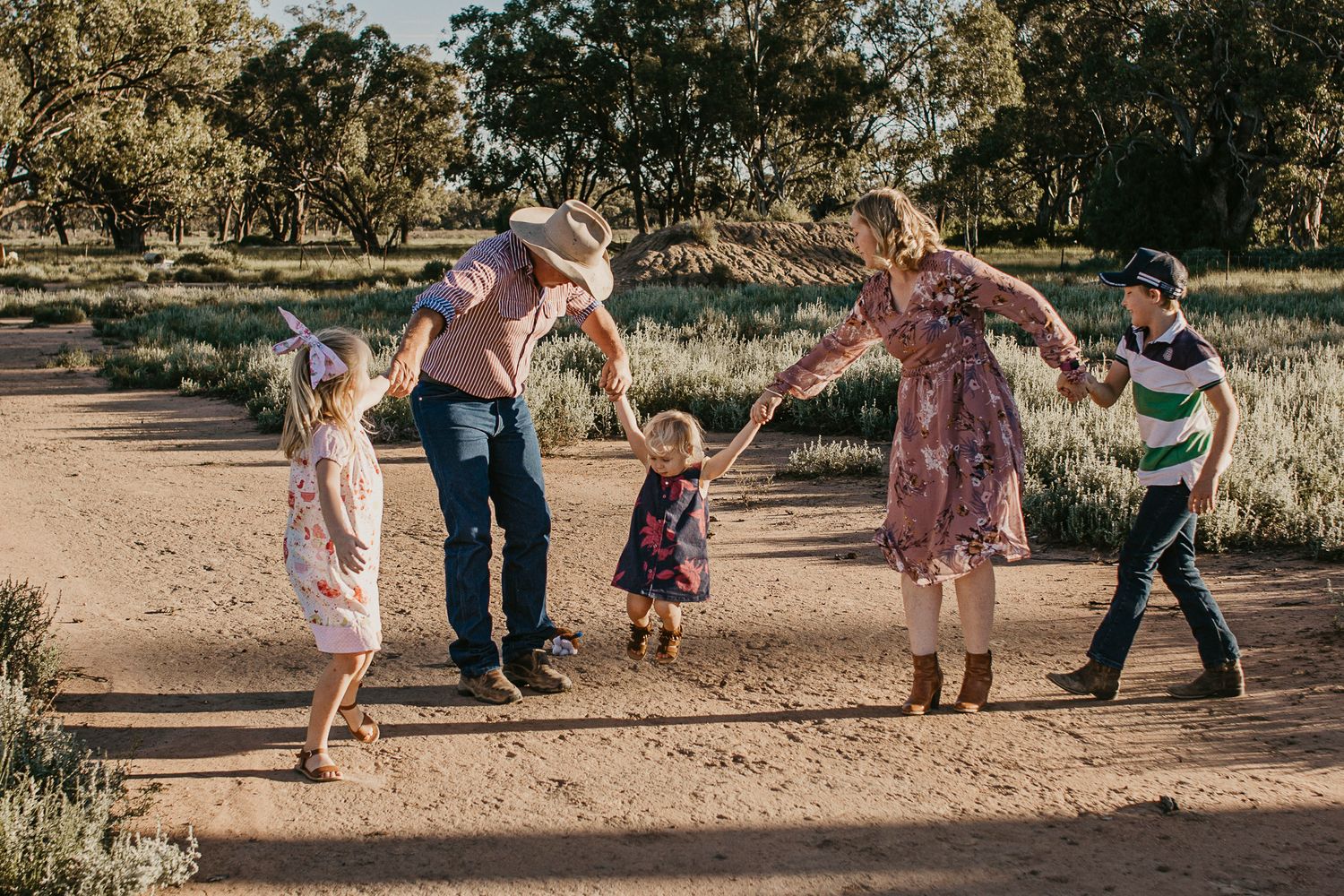 Rural family in a paddock all holding hands watching a little girl swing between paretns