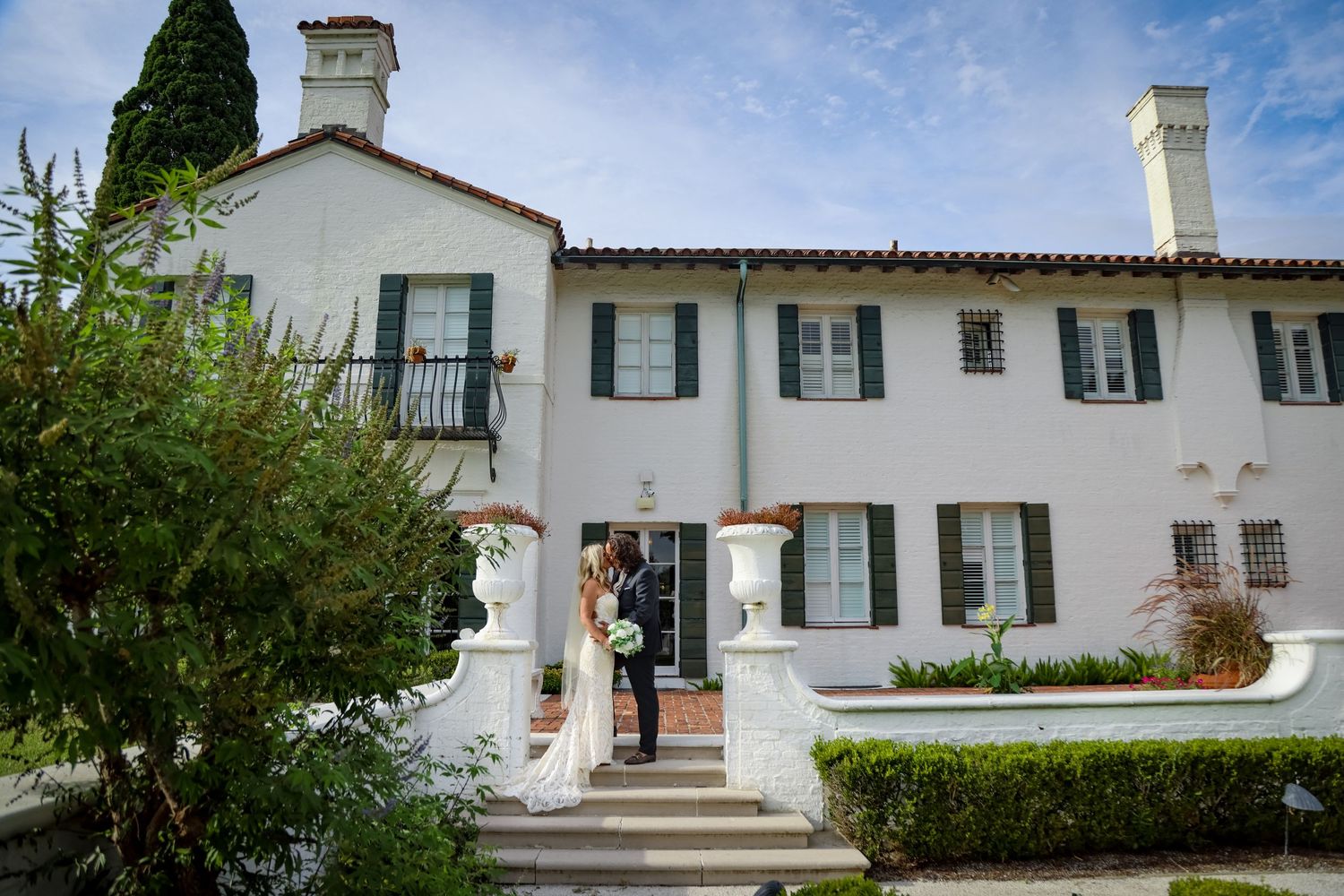 Elegant white Spanish-style building entrance with black shutters and landscaping.