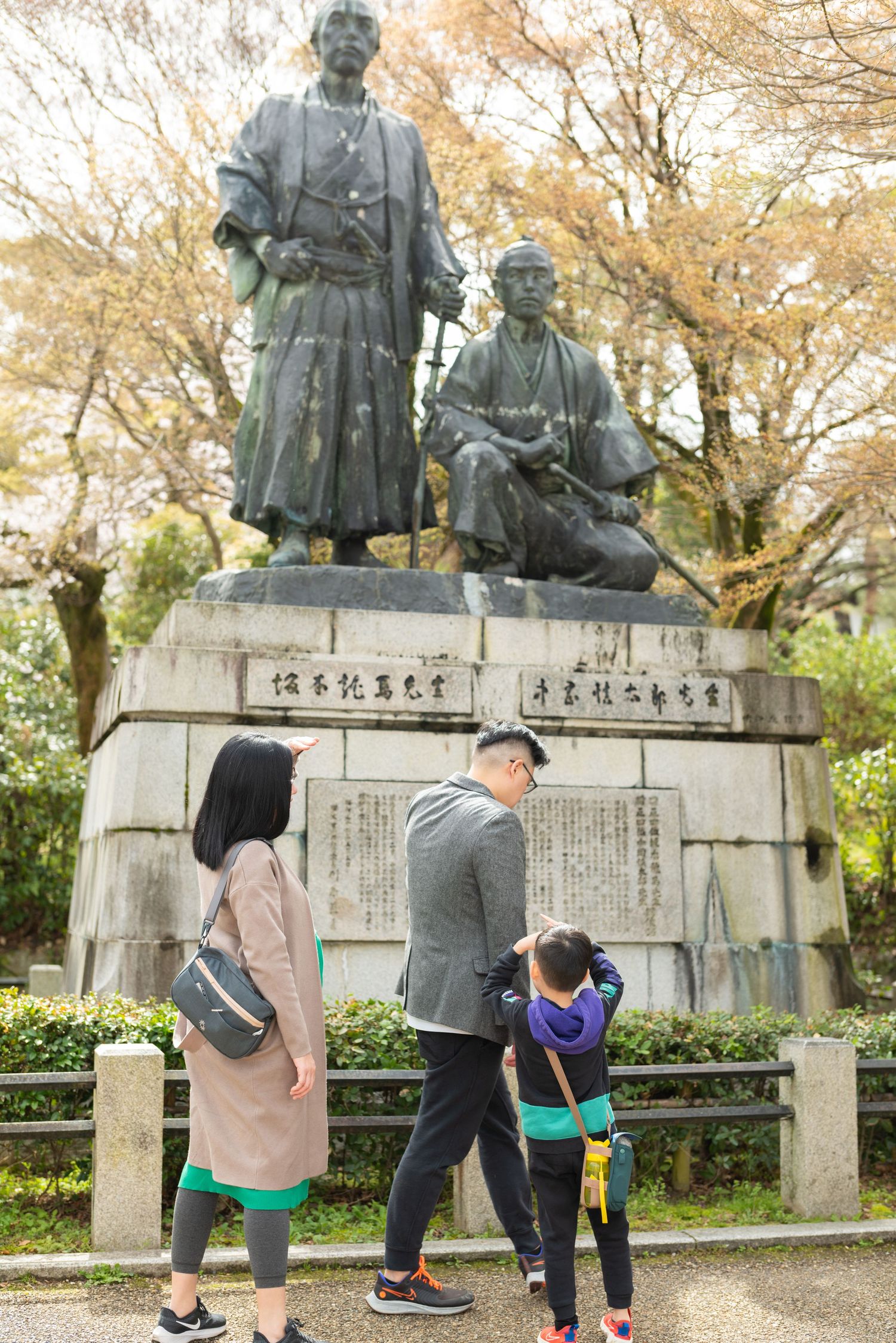 Family with child viewing bronze samurai statues in a Japanese park during autumn.