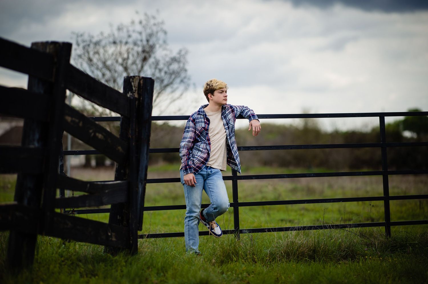 Person sits casually on black wooden fence in countryside setting.