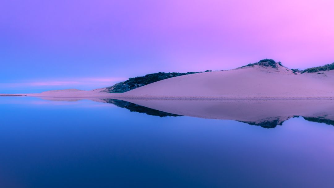 Tranquil mountain landscape reflecting in still waters during twilight with purple and blue hues.