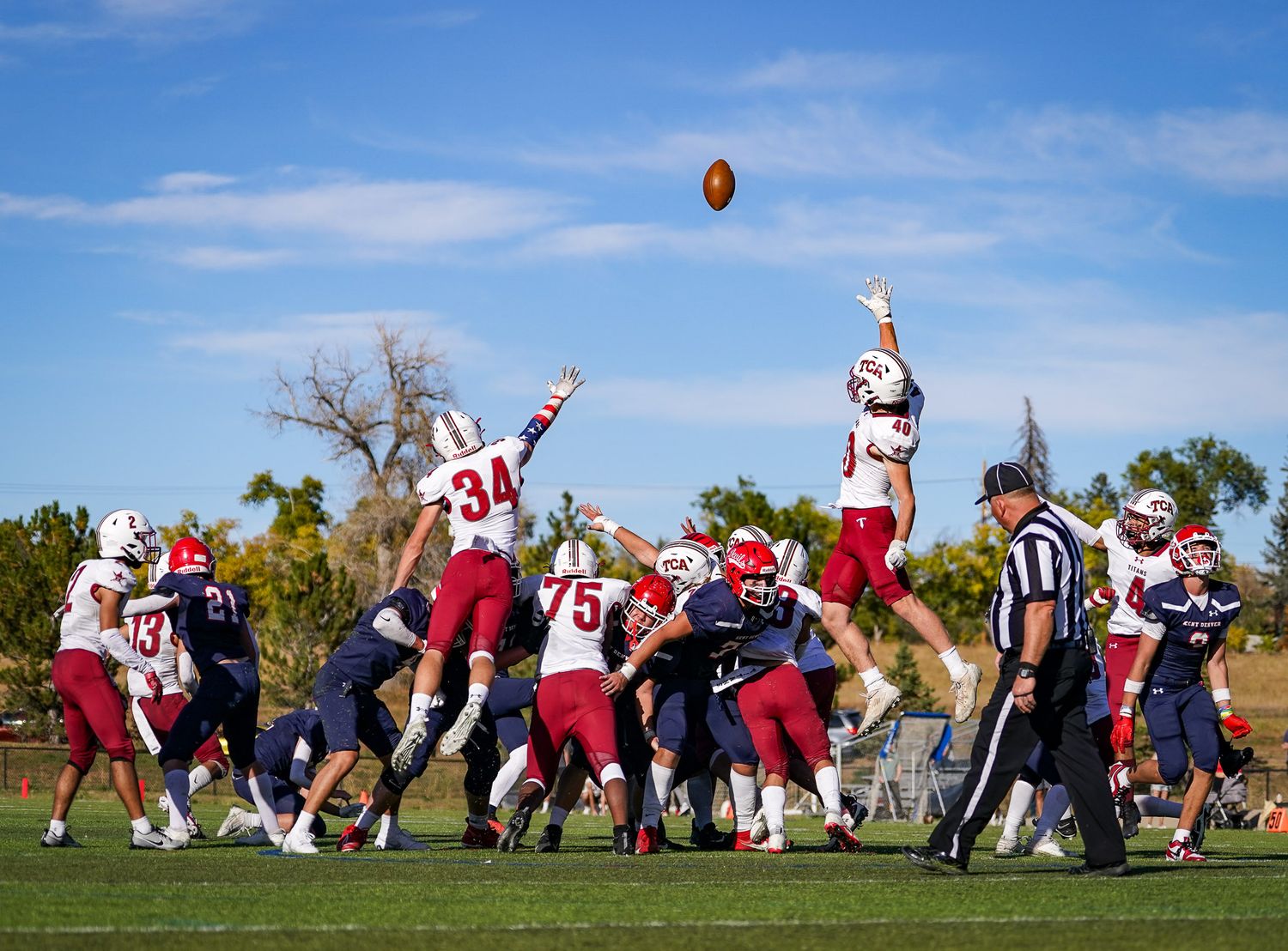 Football players jump to catch a ball during a game under blue sky.