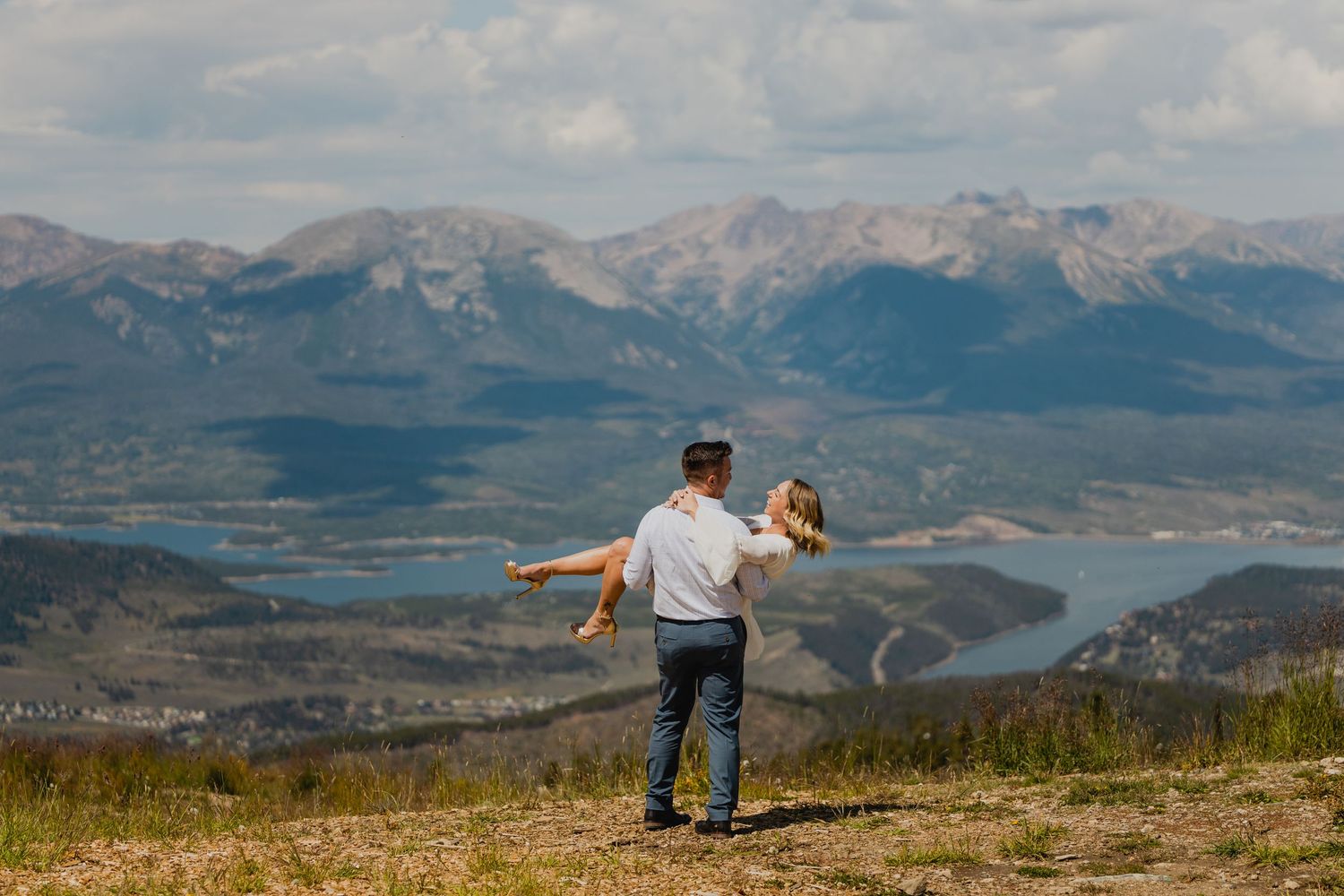 Person spins partner on mountain summit with dramatic valley and mountain range backdrop.