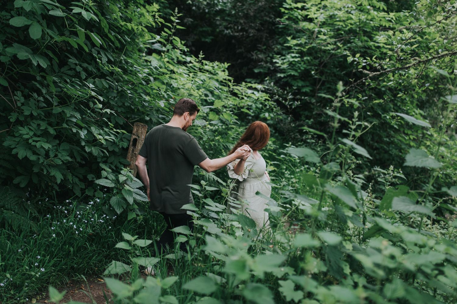Couple walks through lush green forest holding hands on summer day.