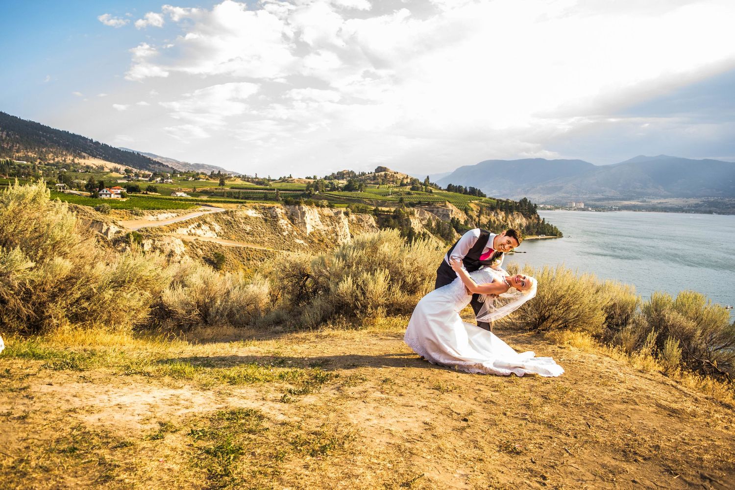 Romantic mountain lakeside scene with dramatic dip pose against natural landscape.