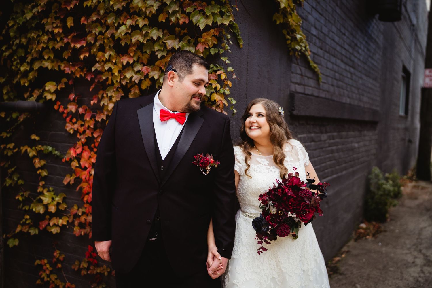 A couple walking together against a brick wall covered in colorful autumn ivy.